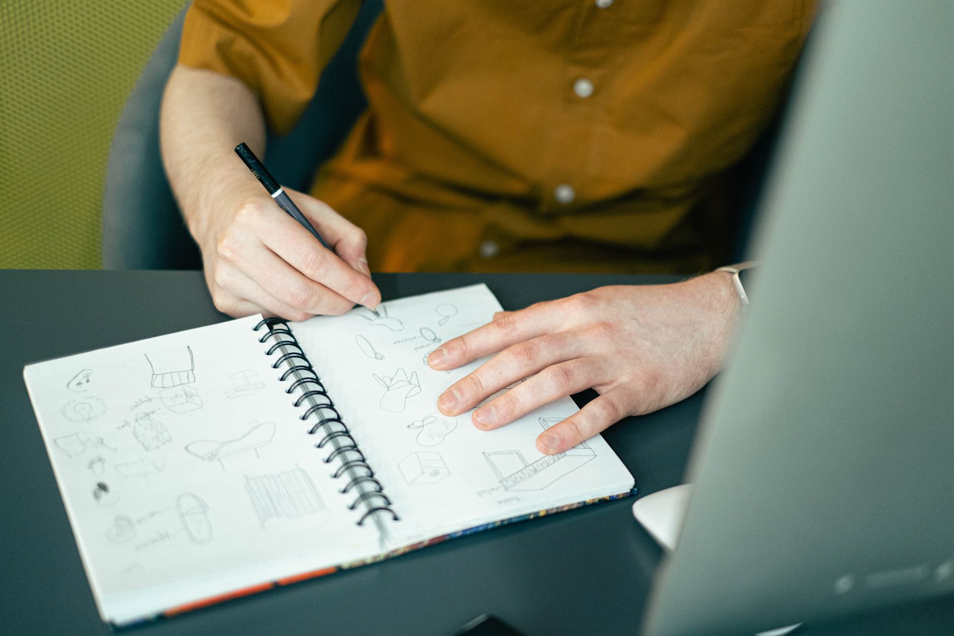 Close-up of someone sketching a plan in a spiral notebook at a desk