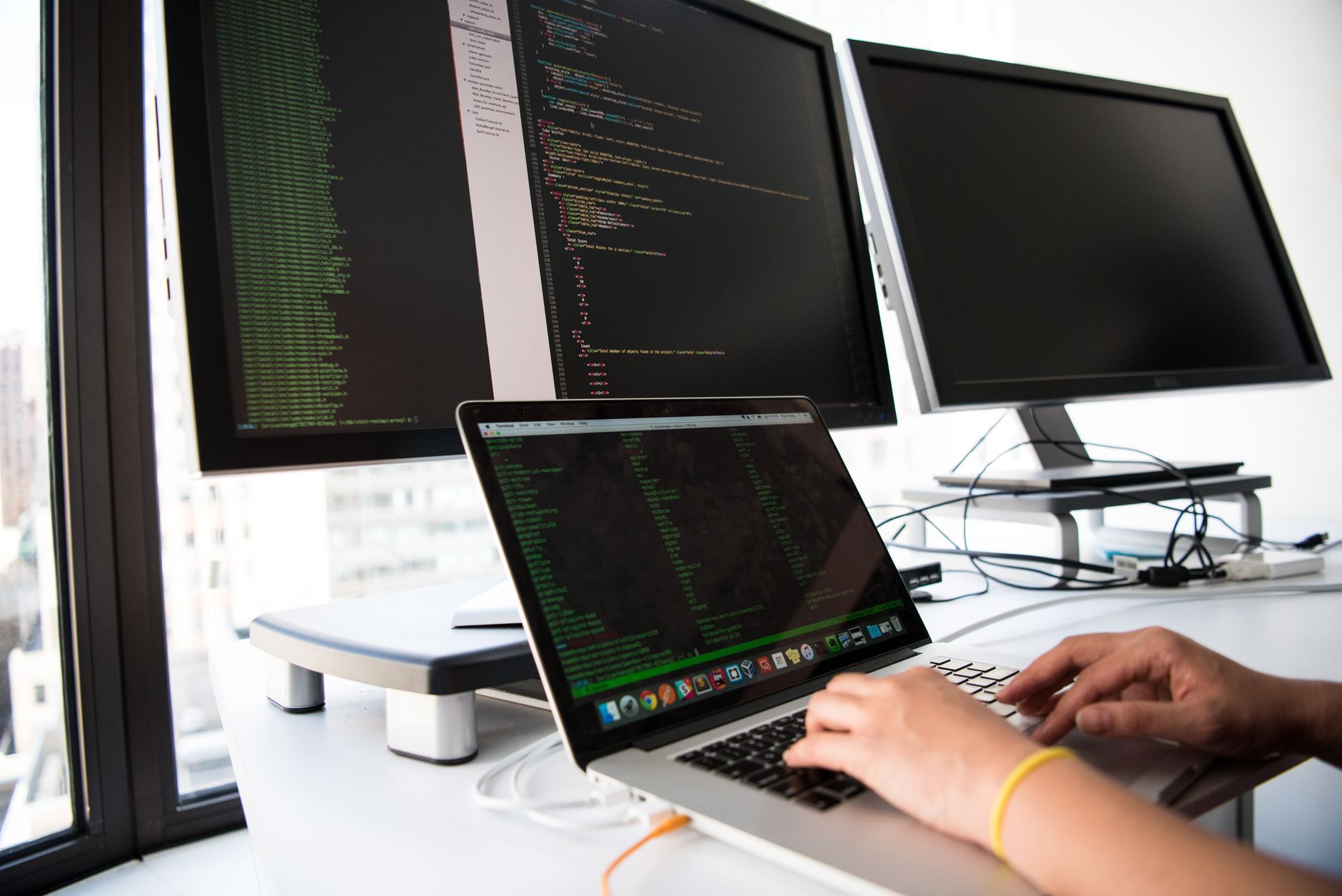Developer typing on a laptop in front of several monitors