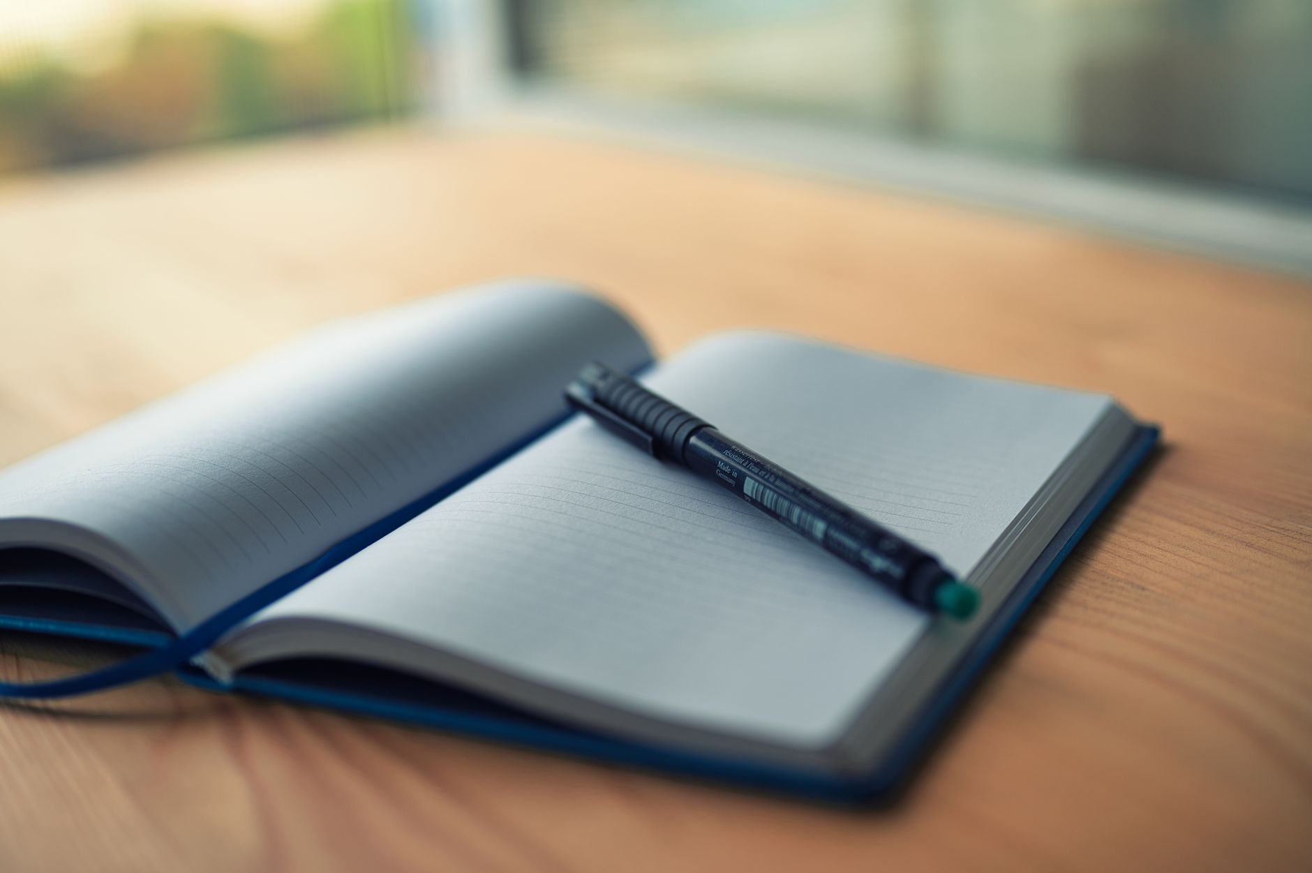 Open lined notebook with a pen resting on a wooden desk
