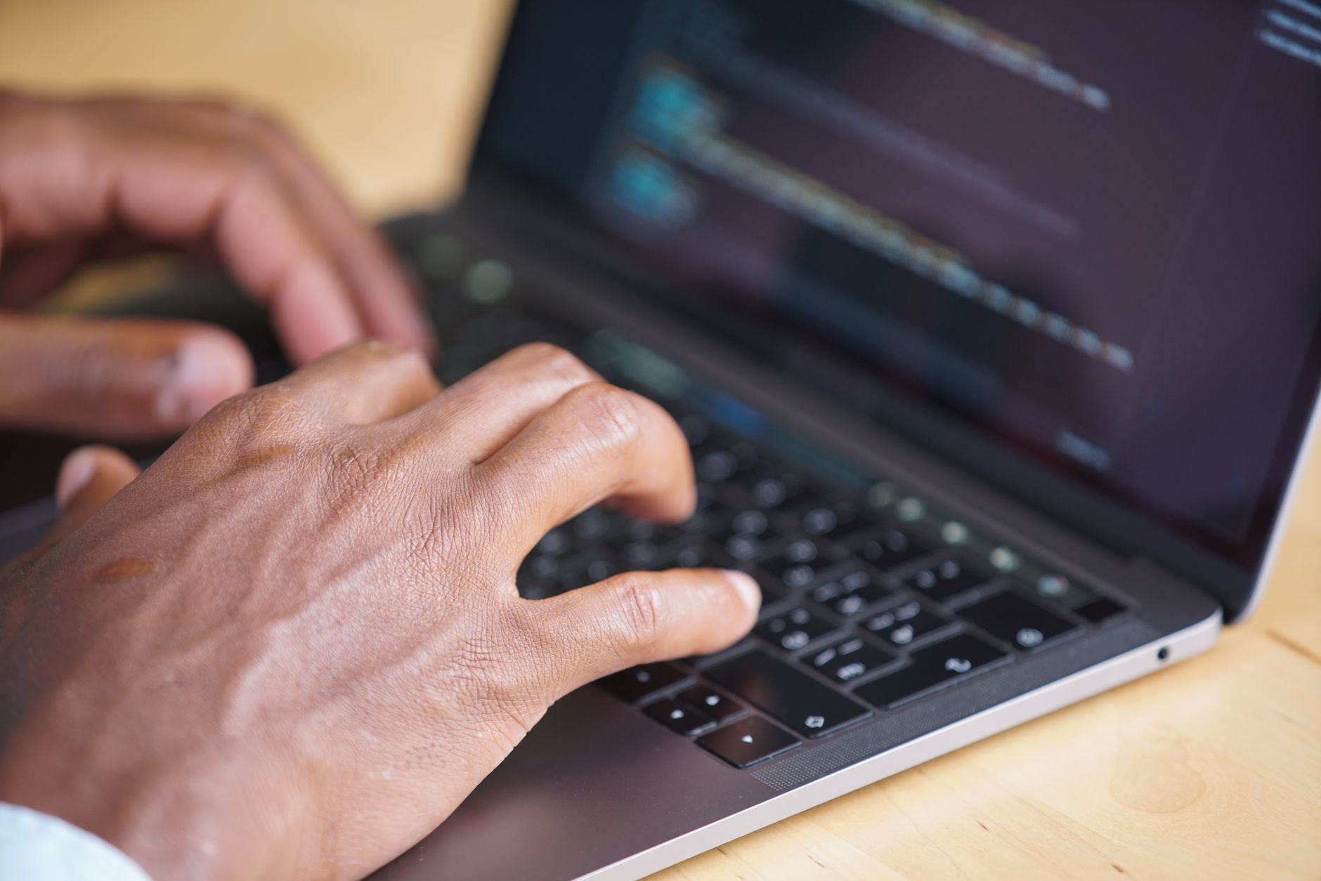 Hands typing on a laptop with code displayed on the screen
