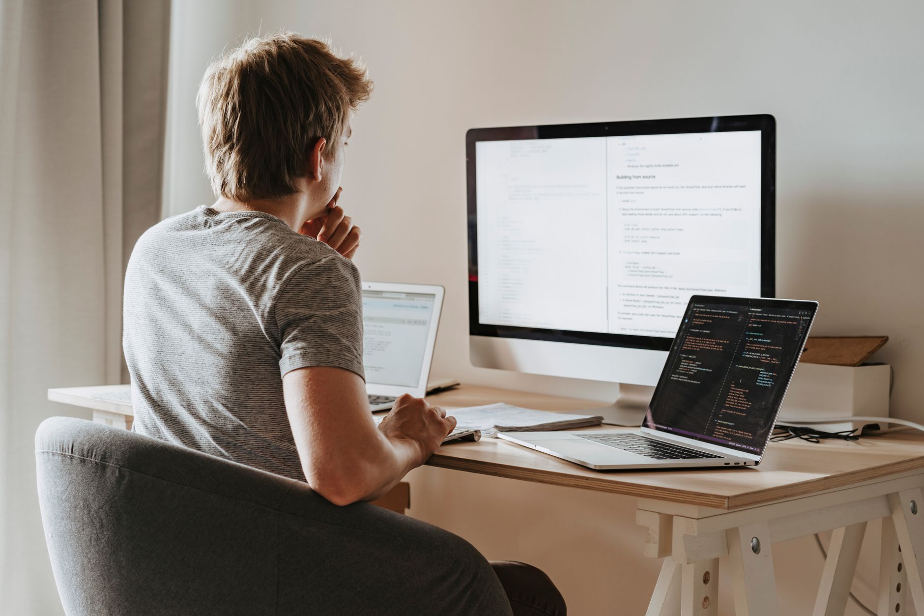 Developer working across two laptops and a desktop monitor