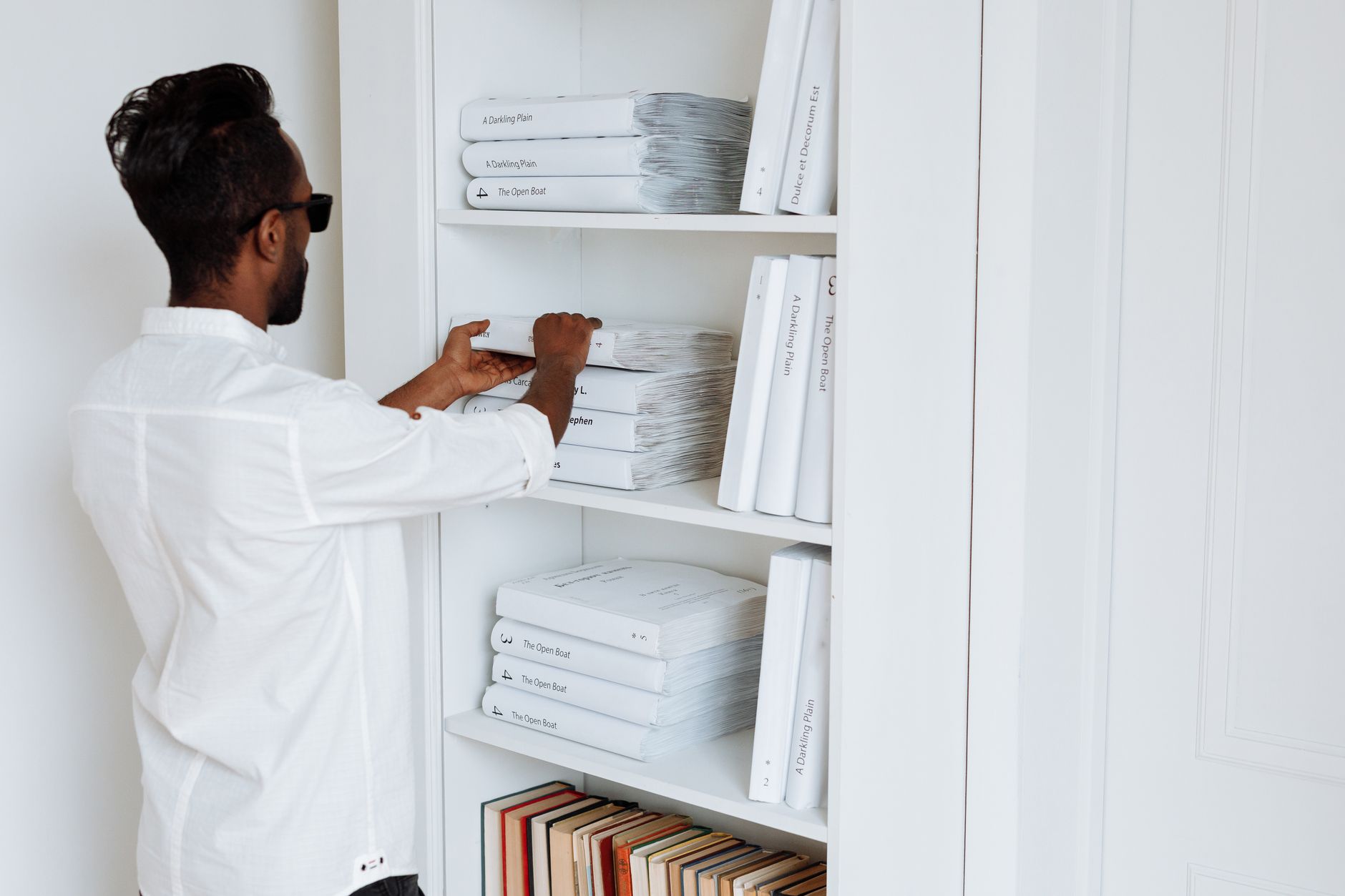 Someone arranging books on minimalist white shelves