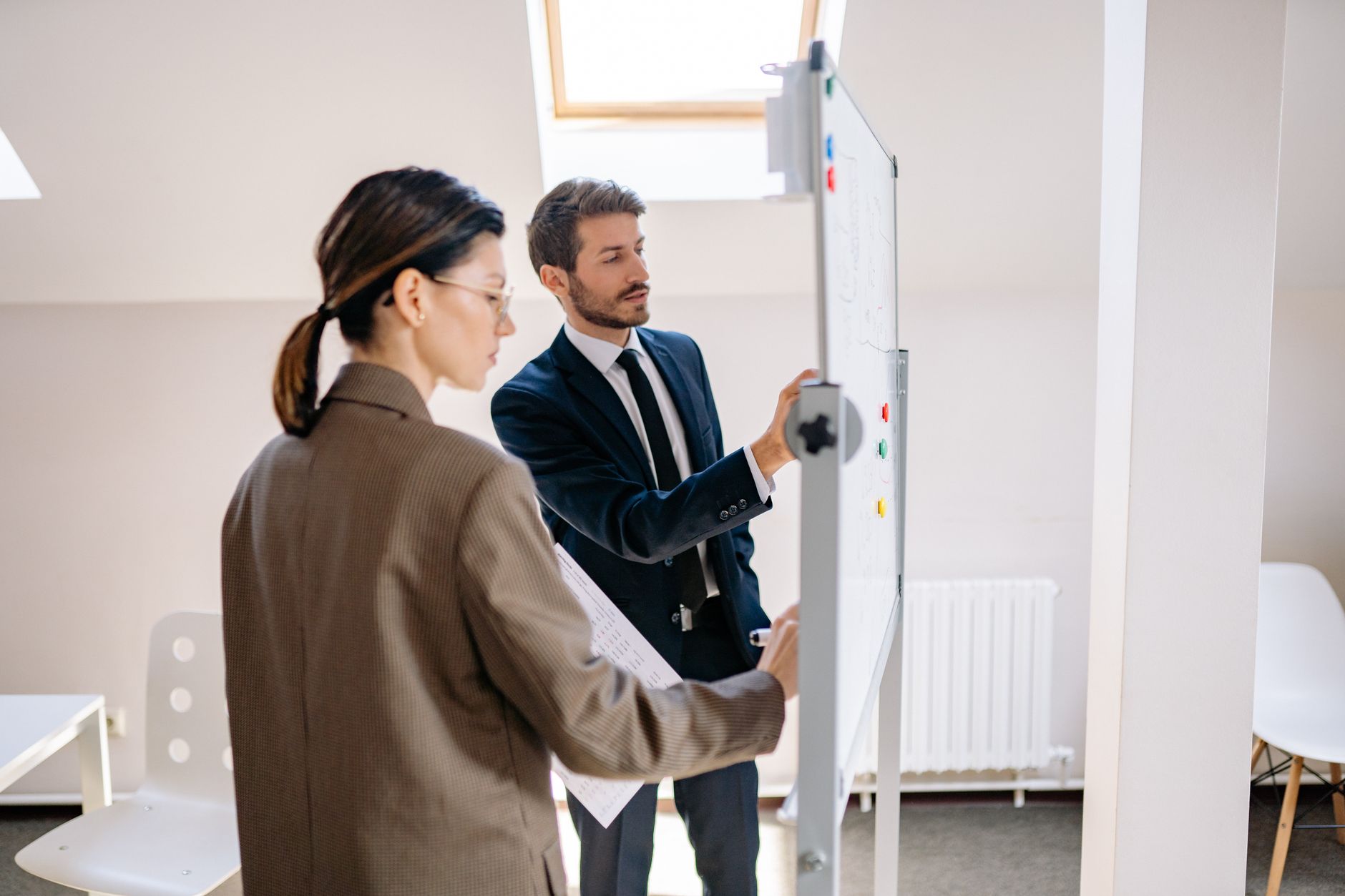 Two colleagues discussing strategy on a whiteboard in a modern office