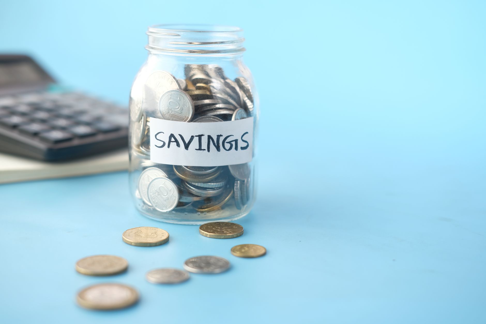 Glass savings jar filled with coins next to a calculator